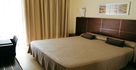 Ein modernes mehrstöckiges Hotel mit Balkonen an jedem Stockwerk, darunter ein Poolbereich mit Sonnenschirmen und entspannten Gästen bei klarem Himmel.