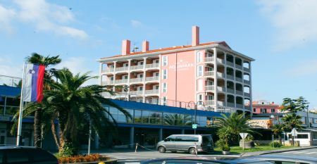 Außenansicht des Hotels Aquapark Zusterna mit rosa Fassade, Balkonen und der slowenischen Flagge.