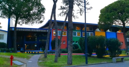 Bunte Fassade der Piscina Olimpica im Bella Italia & EFA Village, umgeben von Pinien und Grünflächen