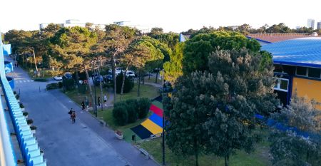 Bunte Fassade der Piscina Olimpica im Bella Italia & EFA Village, umgeben von Pinien und Grünflächen