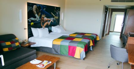 Hotelgebäude mit mehreren Balkonen, neben einer roten Laufbahn und umgeben von Palmen.