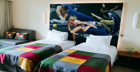 Hotelgebäude mit mehreren Balkonen, neben einer roten Laufbahn und umgeben von Palmen.