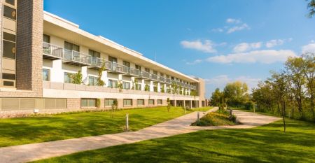 Außenansicht des Hotels Akademia mit gepflegtem Garten und modernen Balkonen. Sonniger Tag und einladende Atmosphäre.
