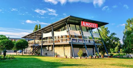 Außenansicht des Hotels Amstel Hattyu Fogado mit moderner Architektur, großen Glasfronten und einer grünen Umgebung