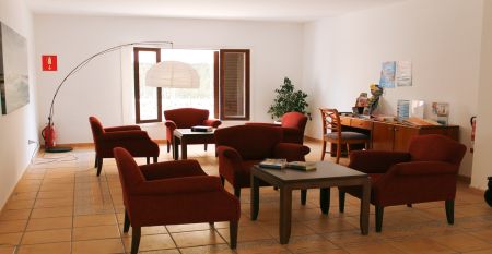 Hotelterrasse mit Pool, umgeben von Liegestühlen und Tischen mit Stühlen, angrenzend an ein gelbliches Gebäude mit Balkonen und großen Glasfenstern.