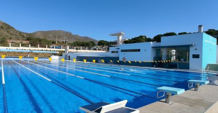 Hotelanlage bei Dämmerung mit beleuchtetem Pool, Sonnenliegen und mehrstöckigem weißen Gebäude.