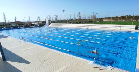 Hotelanlage bei Dämmerung mit beleuchtetem Pool, Sonnenliegen und mehrstöckigem weißen Gebäude.