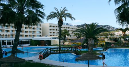 Hotelanlage mit Poollandschaft, Palmen, kleinen Brücken und Blick auf die umliegenden Berge.