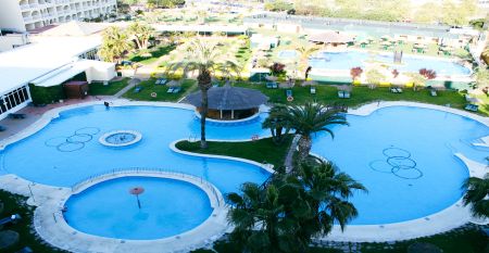 Hotelanlage mit Poollandschaft, Palmen, kleinen Brücken und Blick auf die umliegenden Berge.