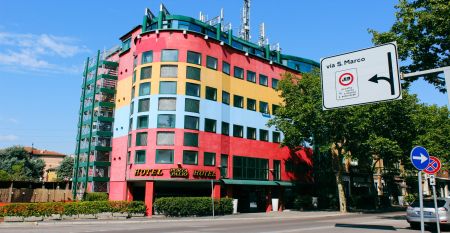 Außenansicht des Hotels Porta Palio mit auffälliger farbenfroher Fassade in Rot, Gelb und Blau, umgeben von Bäumen