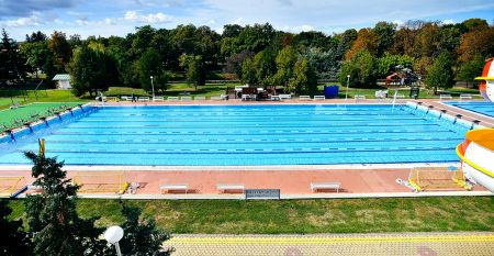 Rotes Hotelgebäude mit dekorativen Balkonen, einem Pool und gepflegter Gartenlandschaft.
