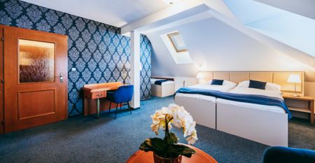 Stilvoll eingerichtetes Hotelzimmer mit einem Doppelbett, blauer Wandtapete und Dachschräge mit Fenster.