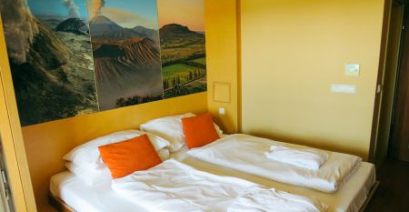 Ein helles Zimmer mit einem Doppelbett, orangen Kissen und einer großen Wanddekoration mit Naturmotiven.