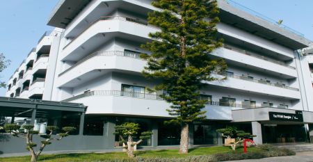 Außenansicht eines modernen Hotelgebäudes mit Balkonen und einem begrünten Vorgarten.