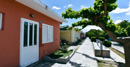 Fußweg auf der Anlage mit bunten Unterkunftshäusern umrahmt von Bäumen im Sport Camp in Loutraki, Korinthia