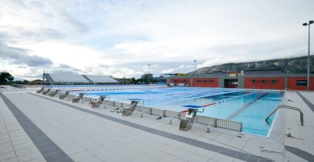 Fußweg auf der Anlage mit bunten Unterkunftshäusern umrahmt von Bäumen im Sport Camp in Loutraki, Korinthia