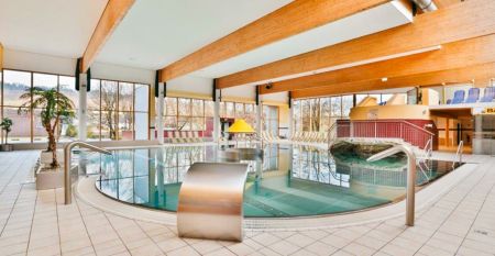 Außenansicht des Sporthotel Kapfenberg mit moderner Fassade und Hotelbeschriftung, im Hintergrund eine Burg auf einem Hügel