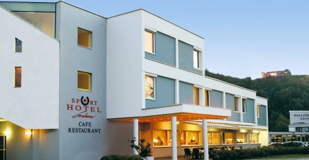Außenansicht des Sporthotel Kapfenberg mit moderner Fassade und Hotelbeschriftung, im Hintergrund eine Burg auf einem Hügel