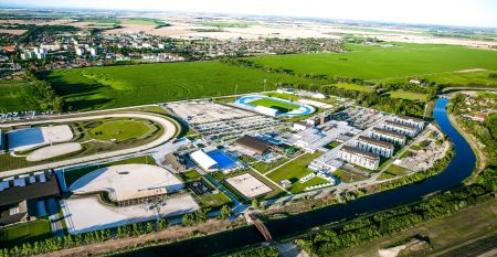 Luftaufnahme des X-Bionic Sportkomplexes mit Schwimmbad, Reitanlage, Leichtathletikstadion und Sportplätzen in grüner Landschaft.