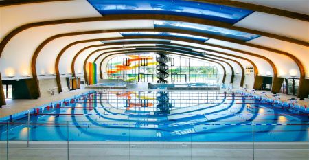 Luftaufnahme des X-Bionic Sportkomplexes mit Schwimmbad, Reitanlage, Leichtathletikstadion und Sportplätzen in grüner Landschaft.