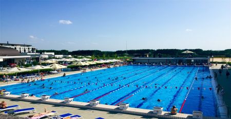 Luftaufnahme des X-Bionic Sportkomplexes mit Schwimmbad, Reitanlage, Leichtathletikstadion und Sportplätzen in grüner Landschaft.