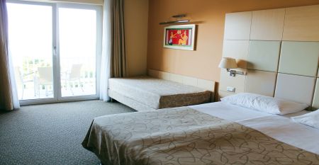 Außenansicht des gelben Gebäudes des Hotels San Simon Dependance, umgeben von Bäumen und Sträuchern.