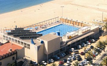 Außenansicht des Hotels mit Balkonen und einem großzügigen Poolbereich mit Liegestühlen und Holzboden.