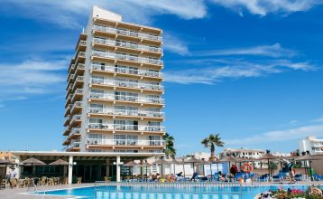 Ein modernes mehrstöckiges Hotel mit Balkonen an jedem Stockwerk, darunter ein Poolbereich mit Sonnenschirmen und entspannten Gästen bei klarem Himmel.