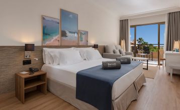 Modernes Hotelgebäude bei Nacht mit beleuchtetem Eingang und Kakteen im Vordergrund.