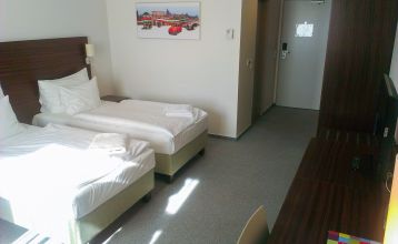 Doppelzimmer im Hotel mit zwei Betten, einem modernen Holzschreibtisch und einem farbenfrohen Wandbild.