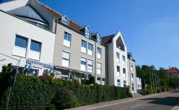 Außenansicht des Hotel im Kaiserpark in Meiningen, Thüringen, neben einer Straße mit einer grünen Hecke und blauem Himmel