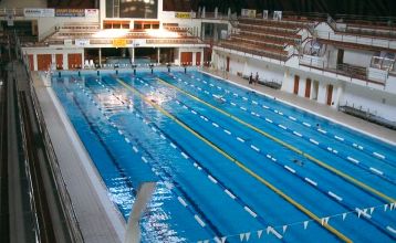 Rotes Hotelgebäude mit dekorativen Balkonen, einem Pool und gepflegter Gartenlandschaft.