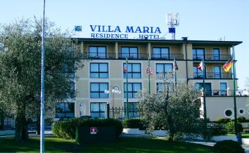 Außenansicht des Hotels Villa Maria mit Balkonen, gepflegtem Garten und mehreren Nationalflaggen vor dem Gebäude