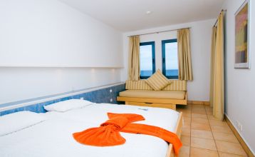 Outdoor-Fitnesskurs mit einer Gruppe von Menschen, die gemeinsam auf Steppern trainieren, vor der Kulisse einer weißen, terrassenförmigen Hotelanlage.