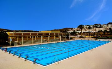 Outdoor-Fitnesskurs mit einer Gruppe von Menschen, die gemeinsam auf Steppern trainieren, vor der Kulisse einer weißen, terrassenförmigen Hotelanlage.