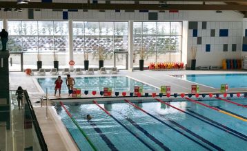 Außenansicht des Ostello Sportivo mit organge-gelb gestrichener Fassade, dahinter ein Fußballplatz und Berge