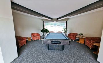 Außenansicht des Sporthotel Kapfenberg mit moderner Fassade und Hotelbeschriftung, im Hintergrund eine Burg auf einem Hügel
