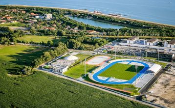 Luftaufnahme des X-Bionic Sportkomplexes mit Schwimmbad, Reitanlage, Leichtathletikstadion und Sportplätzen in grüner Landschaft.