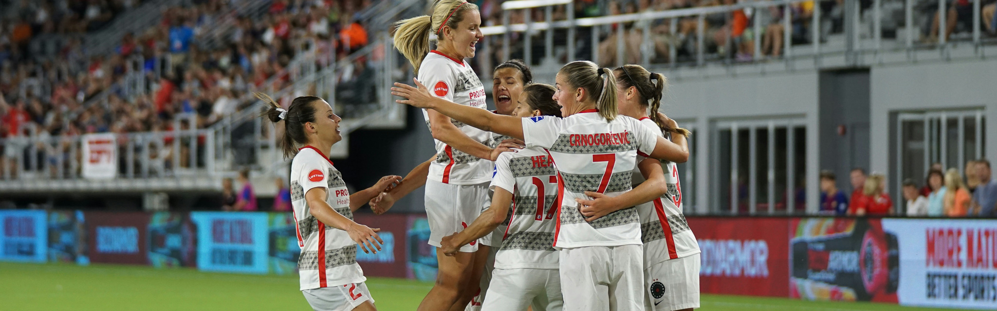 Jubelnde Spielerinnen einer Frauenfußballmannschaft nach einem Tor bei einem Spiel vor großer Zuschauerkulisse.