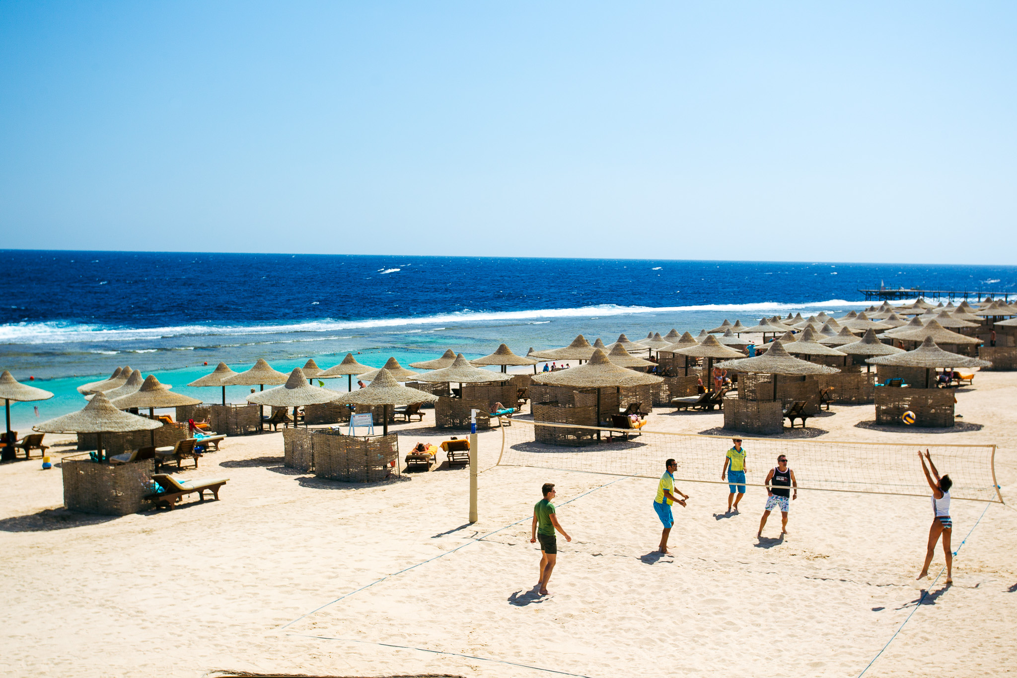 Strand in Ägypten mit Volleyballspielern, Sonnenschirmen und dem klaren blauen Meer im Hintergrund.