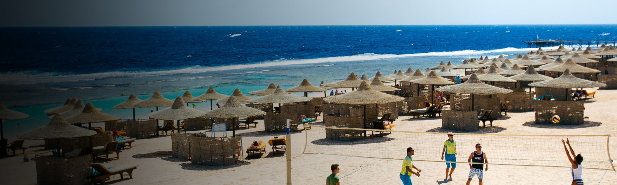 Beachvolleyball-Spiel am Strand in Ägypten mit Sonnenschirmen und dem blauen Meer im Hintergrund.